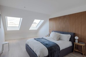 A bedroom with a large bed, two skylights, a wooden headboard, and a bedside table with a lamp. - Soho 2-Bed Penthouse · AC · Sleeps 6 (Greater London)