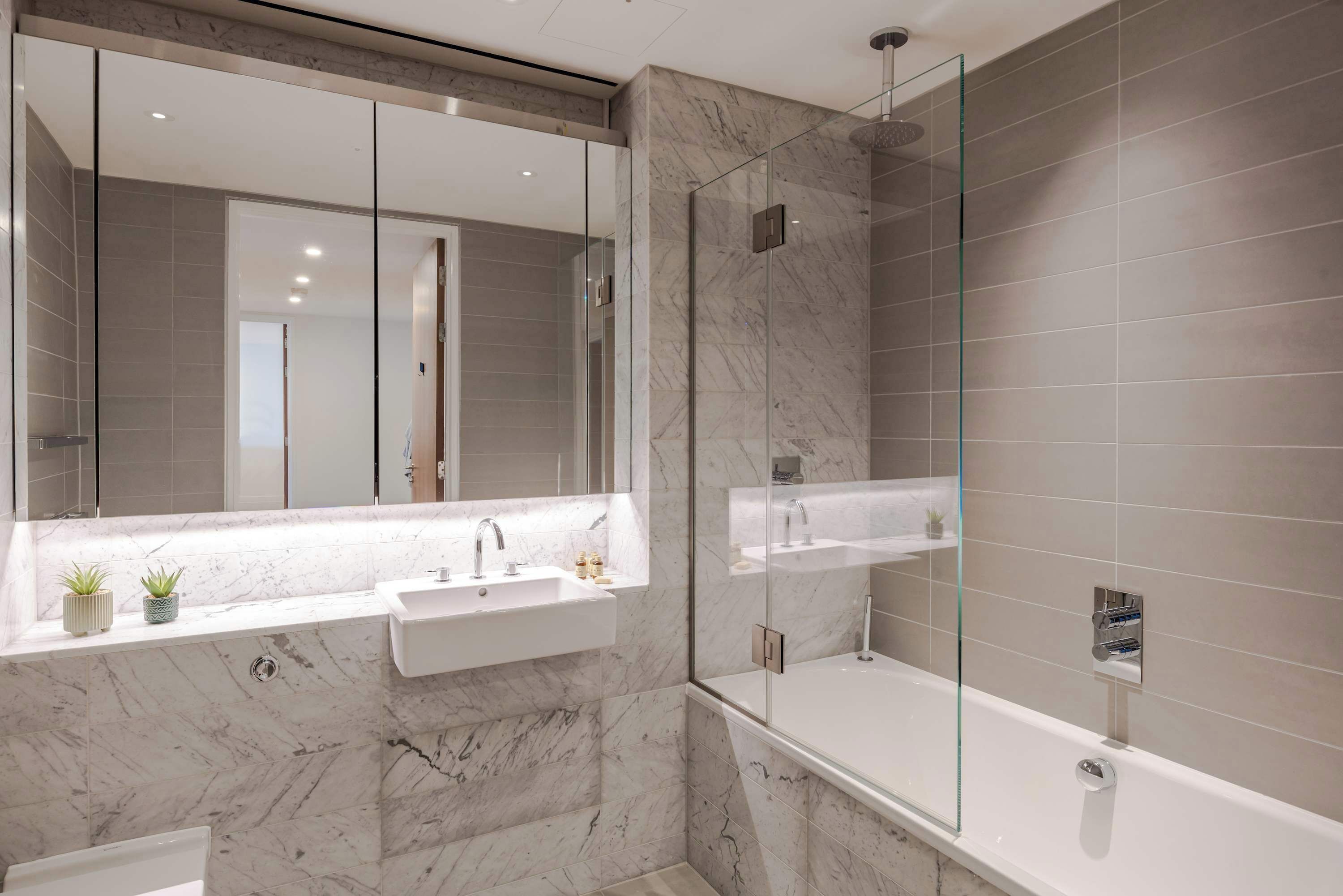 Un baño moderno con ducha de vidrio, lavamanos de mármol y un espejo grande.
