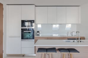 A modern kitchen with white cabinetry, a built-in oven, a microwave, and a sink.