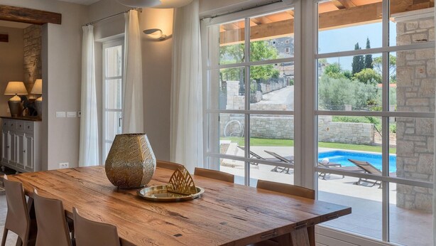 A dining area with a wooden table, chairs, a decorative vase, and a view of a swimming pool and outdoor seating. - Awesome home in Porec (Porec)