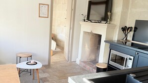 Une cuisine avec un plan de travail en pierre, une table en bois, une chaise blanche, un luminaire suspendu et une cheminée en pierre.