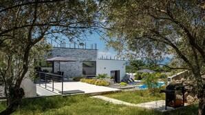 Una villa moderna con fachada de piedra, piscina y zona de patio.