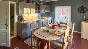 A cozy kitchen with a dining table set for four, wooden chairs, and a window with curtains. - 1 bedroom cozy home in Vormsund (Vormsund)