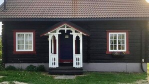 A log cabin with a dark wooden exterior, white trim around the windows and door, and a tiled roof. - 1 bedroom cozy home in Vormsund (Vormsund)