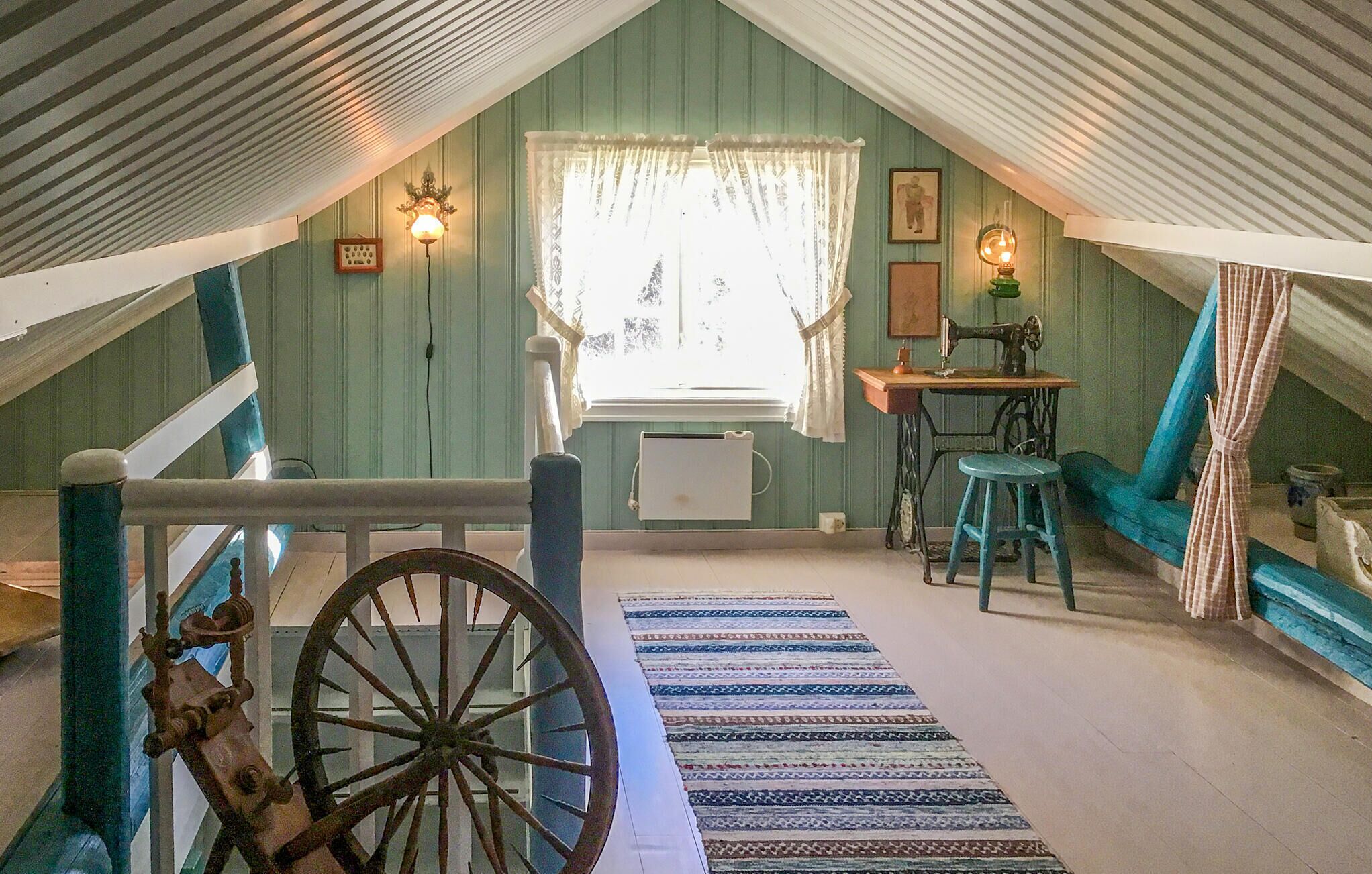 Ein gemütliches Dachzimmer mit einem großen Holzrad, einer Nähmaschine und einem blauen Stuhl.