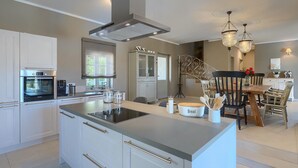 Une cuisine moderne dotée d’un îlot central, d’appareils électroménagers intégrés et d’un coin repas agrémenté d’un lustre.