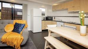 A modern kitchen with wooden cabinets, a white refrigerator, and a dining area with a bench and table. - Yurali apartment is located within walking distance to the town centre. (Jindabyne)