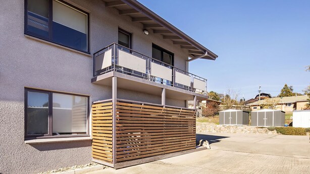 A modern two-story building with a balcony, large windows, and a wooden slatted fence. - Yurali apartment is located within walking distance to the town centre. (Jindabyne)