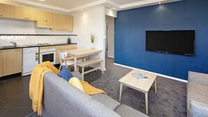 A modern living room with a sofa, coffee table, and a flat-screen TV mounted on a blue wall. - Yurali apartment is located within walking distance to the town centre. (Jindabyne)