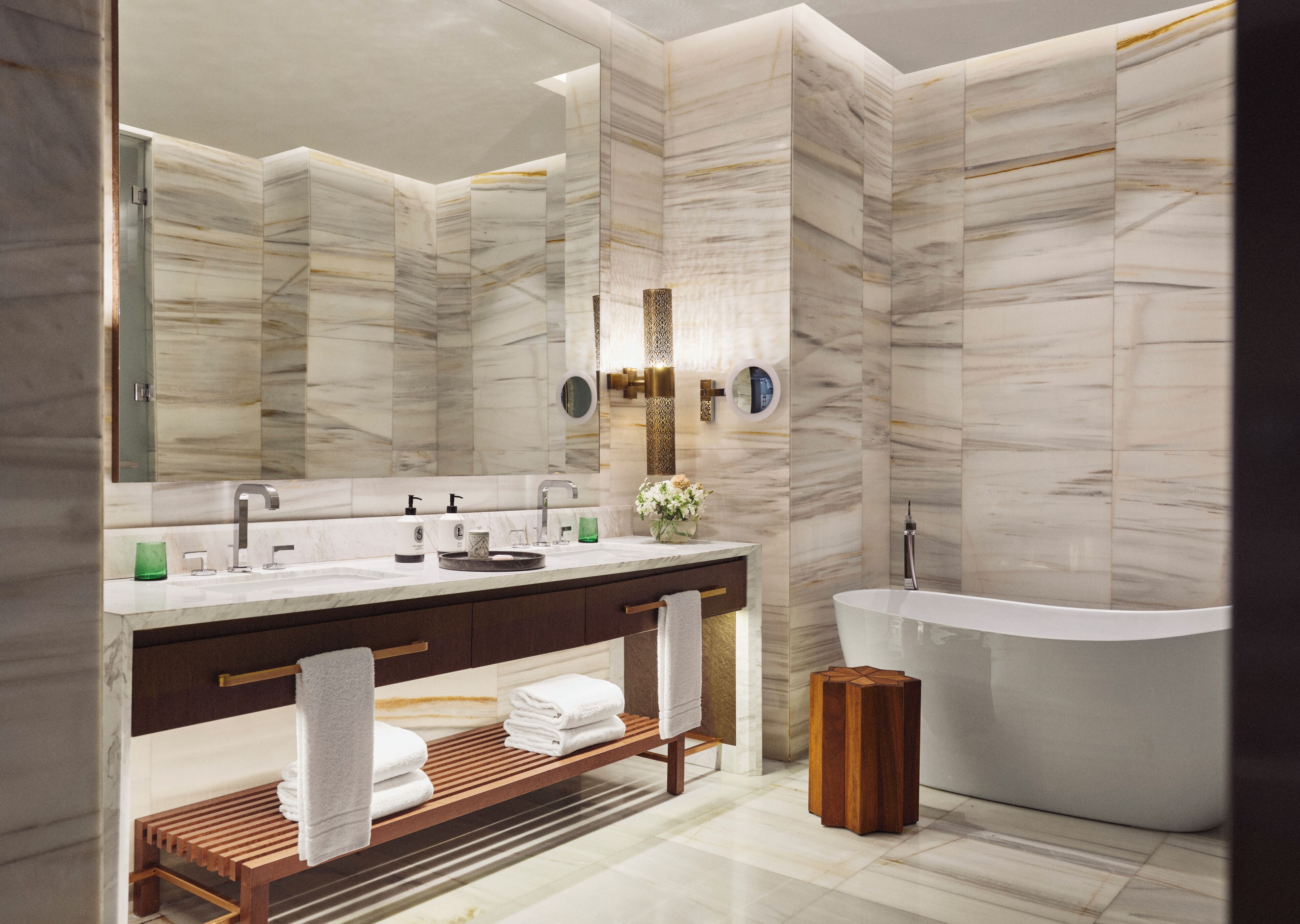 A modern bathroom with a freestanding bathtub, a large mirror, and a vanity with a wooden shelf.
