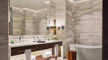 A modern bathroom with a freestanding bathtub, a large mirror, and a vanity with a wooden shelf.