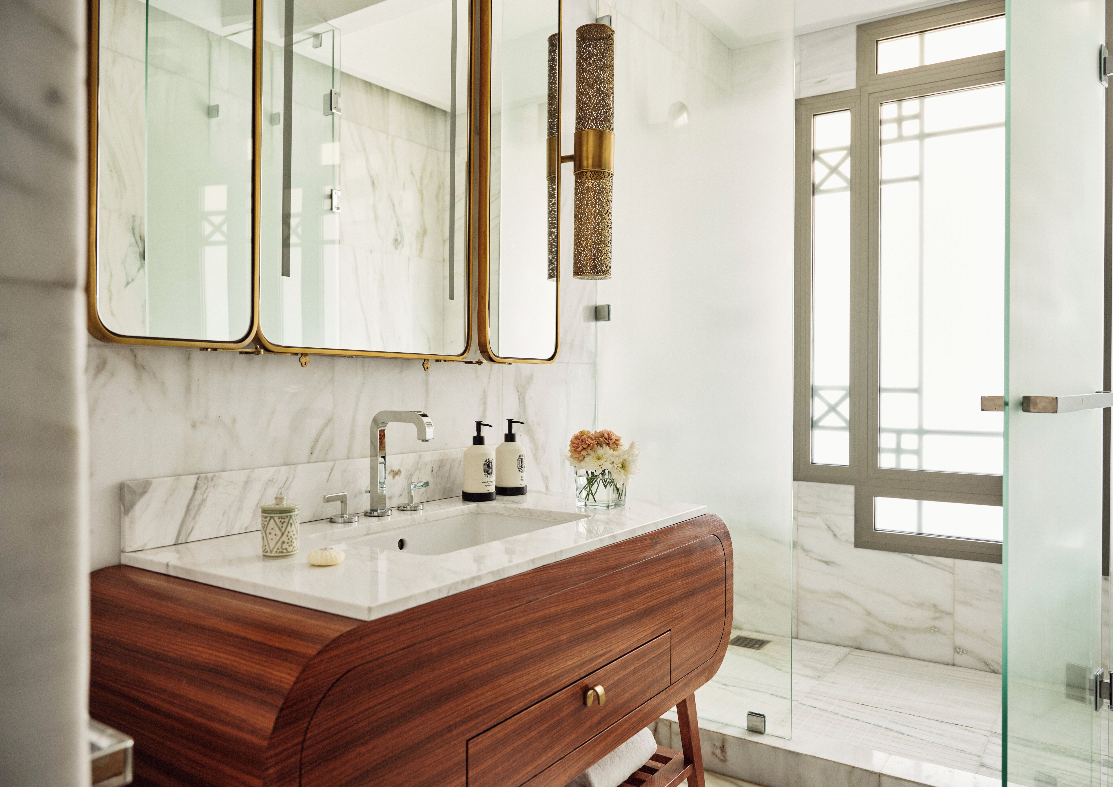 A bathroom with a marble vanity, a wooden cabinet, a glass shower enclosure, and a large mirror with gold frames.