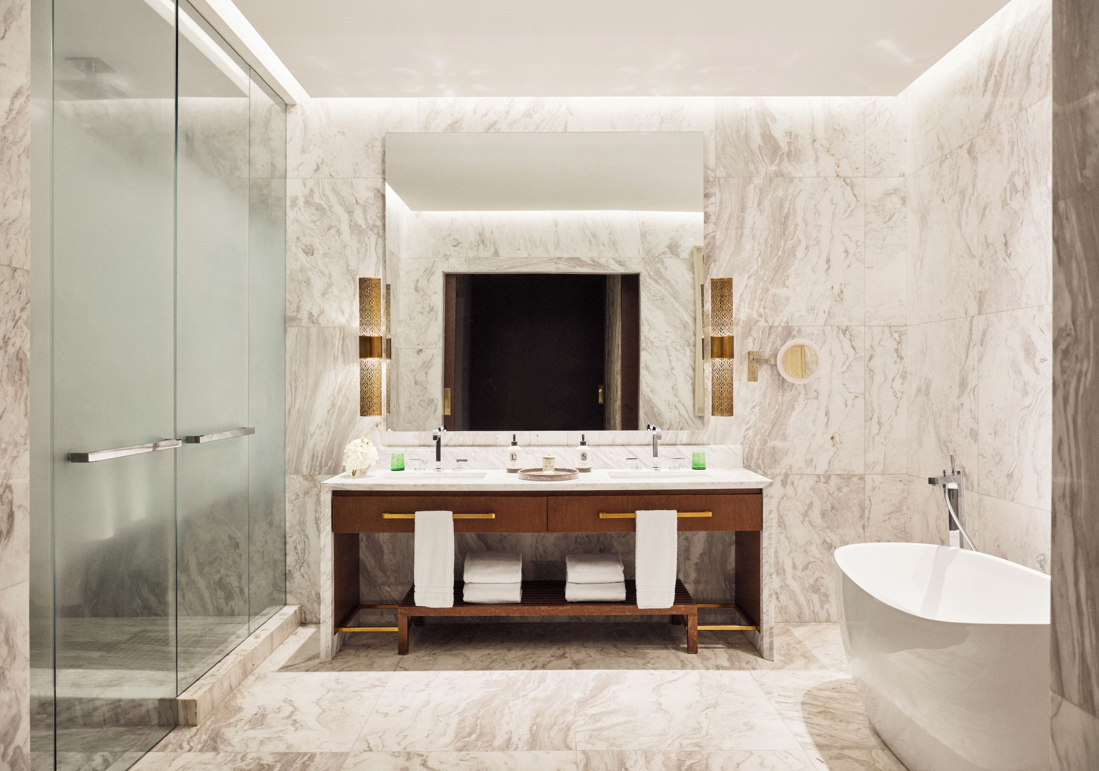 Un baño moderno con cabina de ducha de vidrio, una bañera independiente y un tocador con azulejos de mármol y un espejo grande.