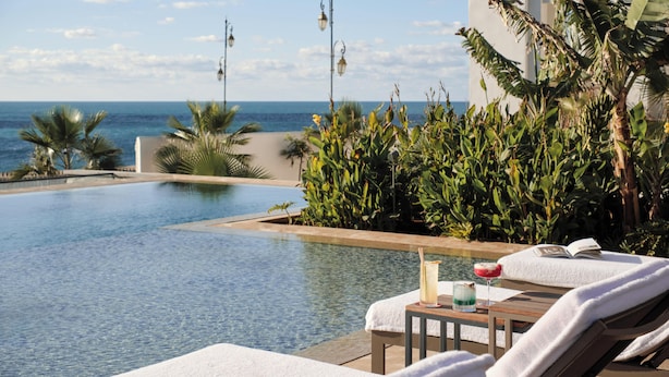 A poolside area with lounge chairs, a small table with a drink, and a view of the ocean. - Four Seasons Hotel Rabat At Kasr Al Bahr (Rabat)