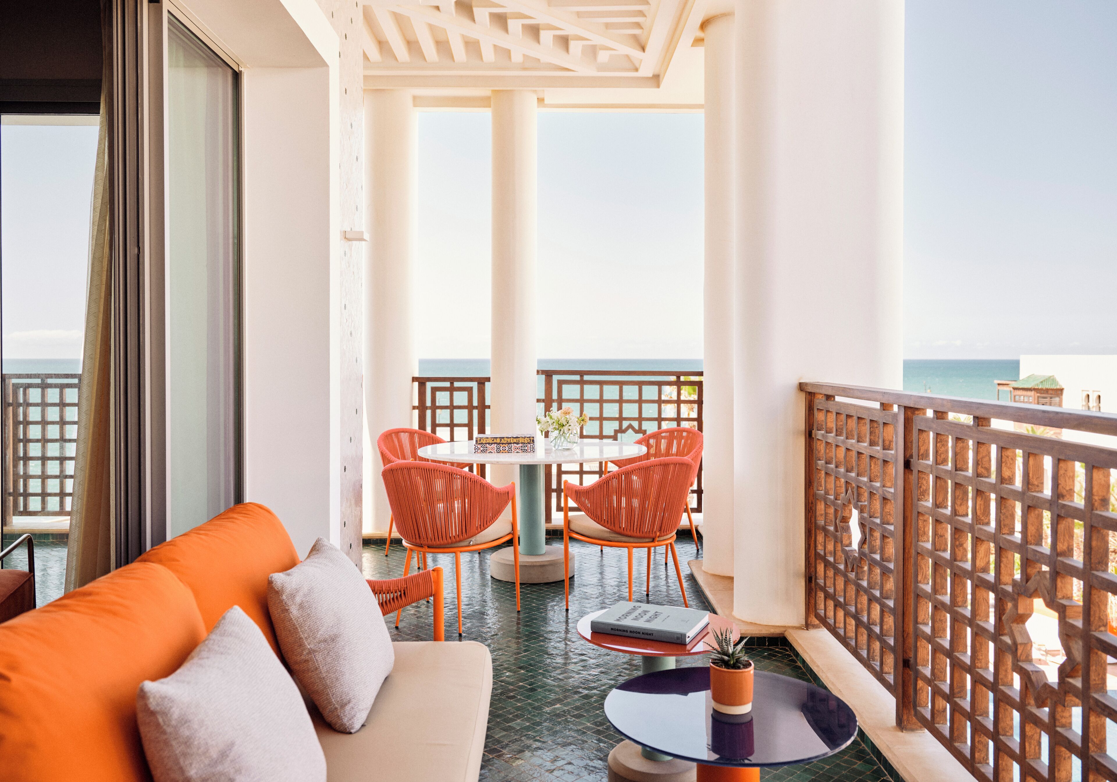 A balcony with a view of the sea, furnished with a sofa, chairs, and a table.