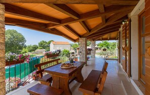 Un patio techado al aire libre con bancos de madera y una mesa, pilares de piedra y vistas del entorno.