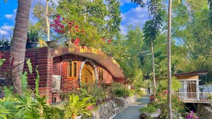 A brick building with a curved archway, surrounded by lush greenery and potted plants.