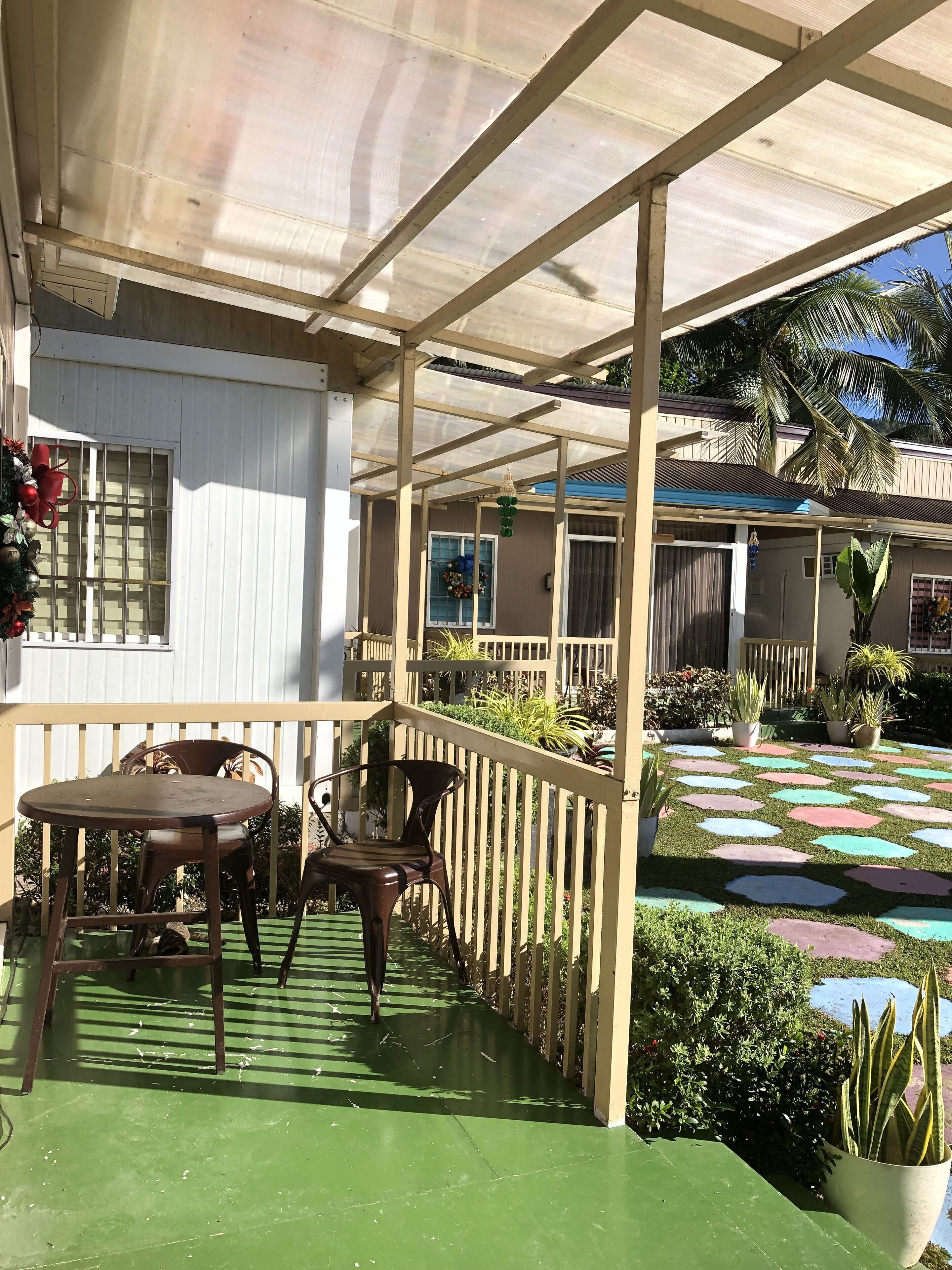 A covered outdoor area with a green floor, a table and chairs, and potted plants.