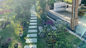 A covered outdoor area with a stone pathway, potted plants, and a seating area with a table and chairs.