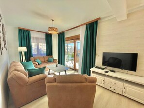 Sala de estar com sofá, mesa de centro, televisão e cortinas.