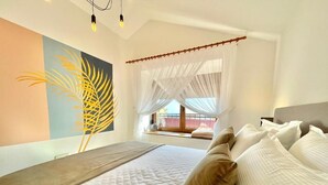 Ein Schlafzimmer mit einem Bett, einem Fenster mit durchsichtigen Vorhängen und einem Wandbild.