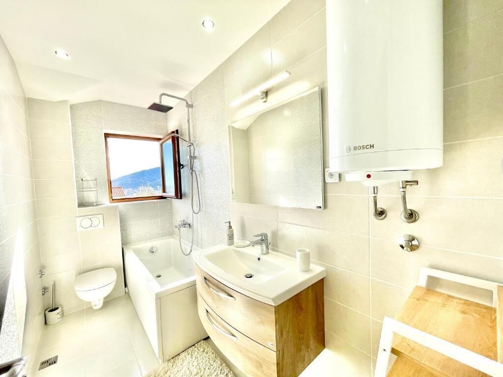 Une salle de bain moderne avec une baignoire, un lavabo et des toilettes. Il y a une fenêtre qui offre une vue sur les montagnes.