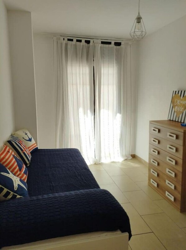 A bedroom with a bed, a dresser, and a window with curtains.