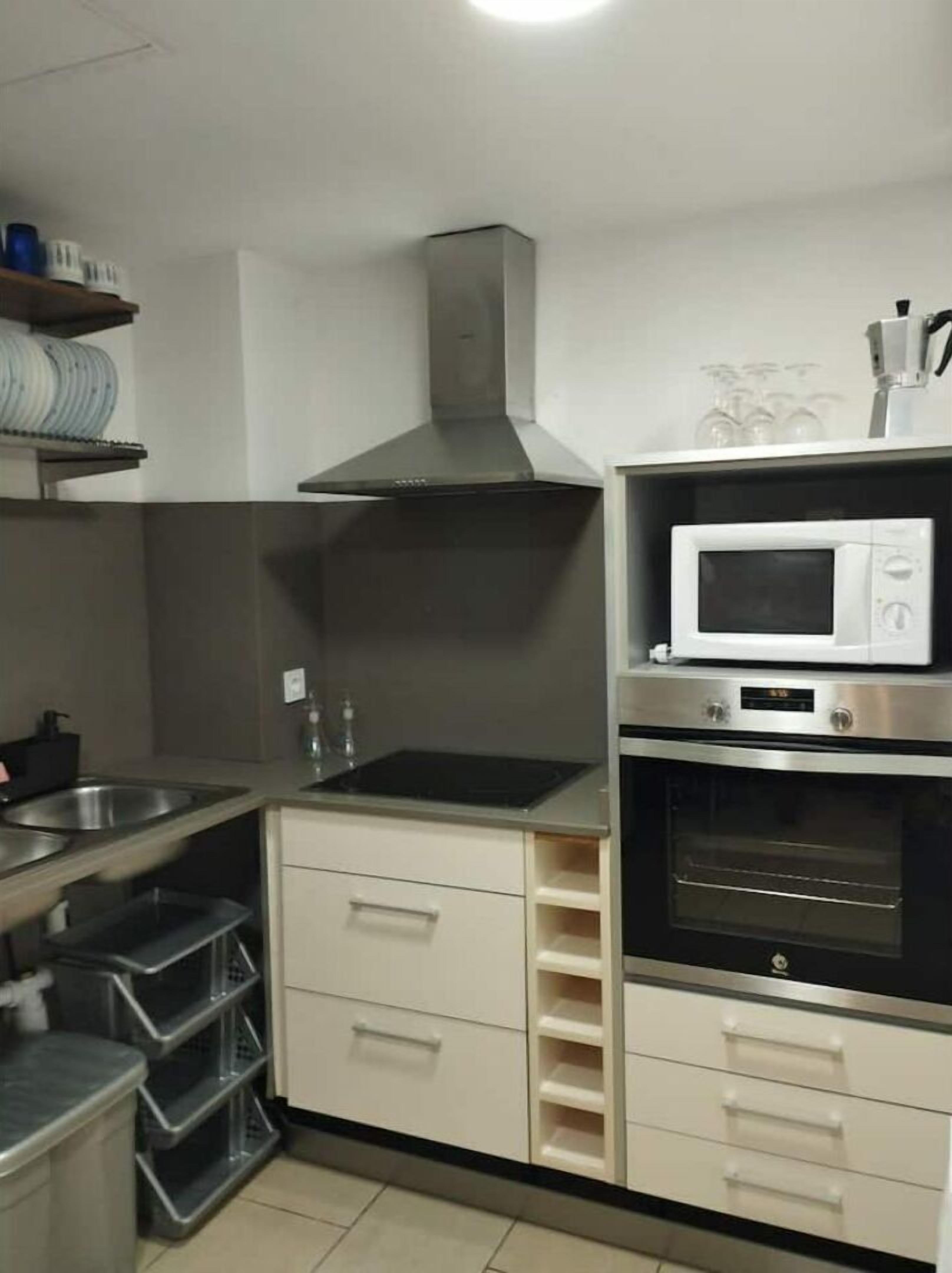 Cocina compacta con campana de acero inoxidable, microondas y horno. Incluye cajones de almacenamiento y un lavamanos con grifo.