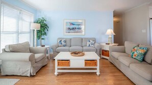 A living room with two sofas, a coffee table, and a painting on the wall. - Sea La Vie Cottage Retreat (Kure Beach)