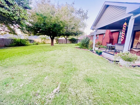 Un patio trasero residencial con césped, un árbol y una casa con porche.