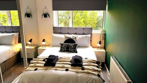 Ein Schlafzimmer mit Bett, Nachttischen, einem Spiegel und einem Fenster mit Blick auf Bäume.