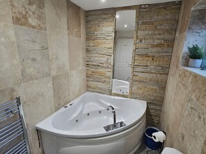 A modern bathroom with a freestanding bathtub, a stone wall, and a mirror.