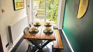Ein Essbereich mit einem Holztisch, gedeckt für vier Personen, mit Blick auf einen Garten durch eine Glastür und einer grünen Wand mit einem dekorativen Element.