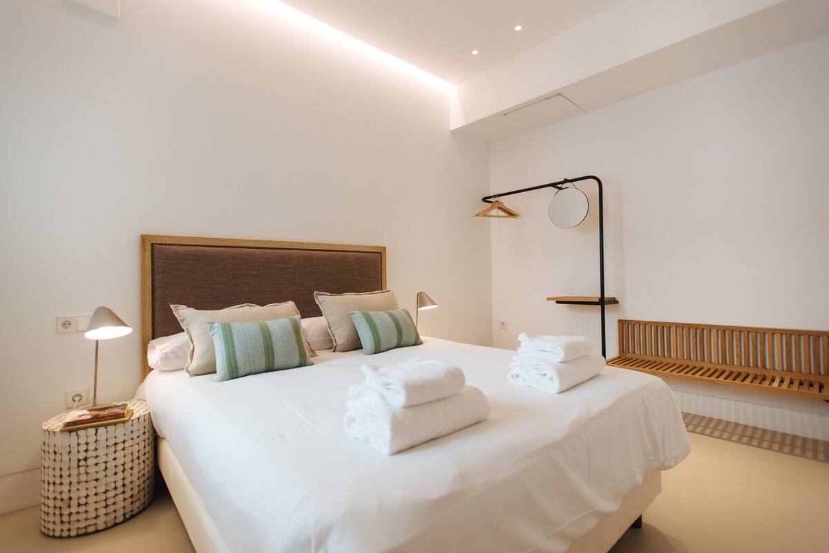 A modern bedroom with a large bed, bedside lamps, and a wooden headboard.