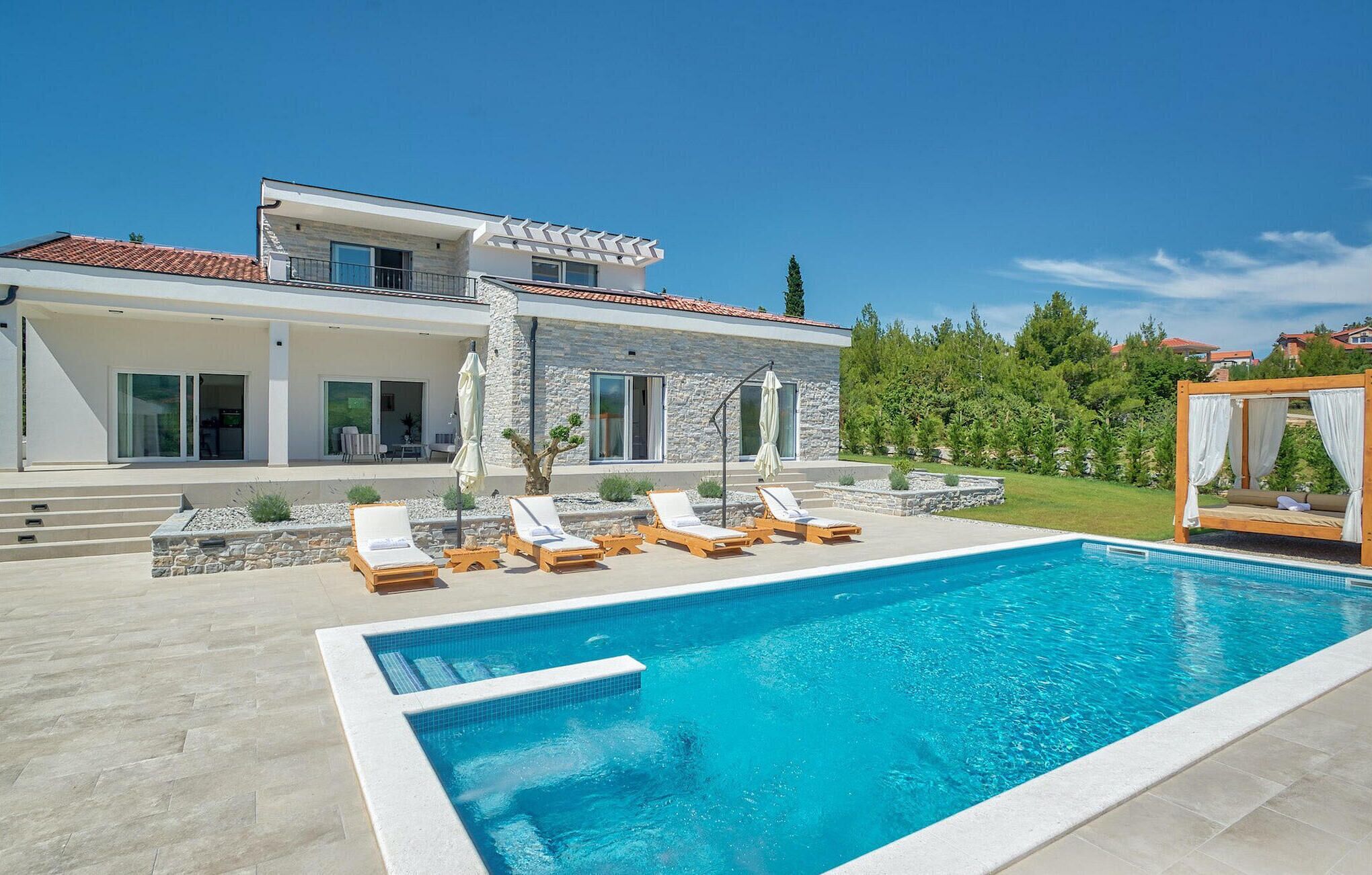 Une maison moderne dotée d’une piscine, d’un espace salon extérieur et d’une façade en pierre.