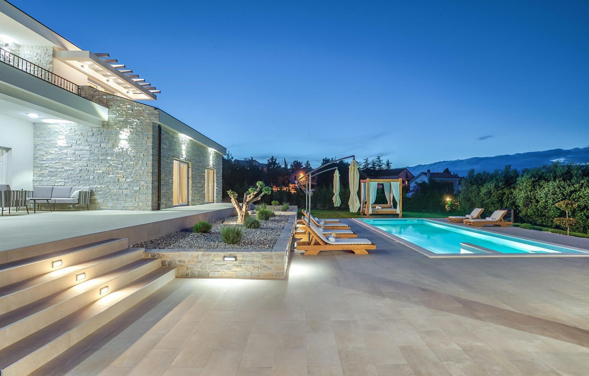Une maison moderne dotée d’une piscine, d’un espace salon extérieur et d’une façade en pierre.