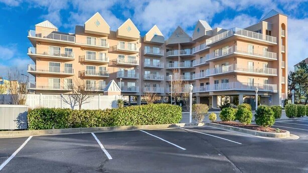 Een meerlaags hotel met een symmetrische gevel, balkons op elke verdieping en een parkeerplaats voor.