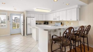 Een moderne keuken met witte kasten, een centraal eiland met barkrukken en inbouwspots.