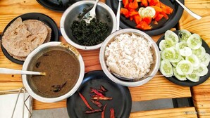 A variety of dishes including rice, vegetables, and a dark soup, arranged on a wooden table. - Khaltaal Camp And Resorts (Chamoli)