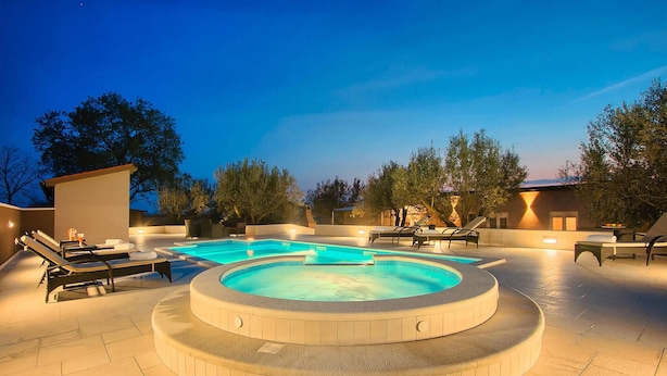 A swimming pool area with lounge chairs and a hot tub, surrounded by trees and buildings. - Gorgeous home in Pula (Pula)