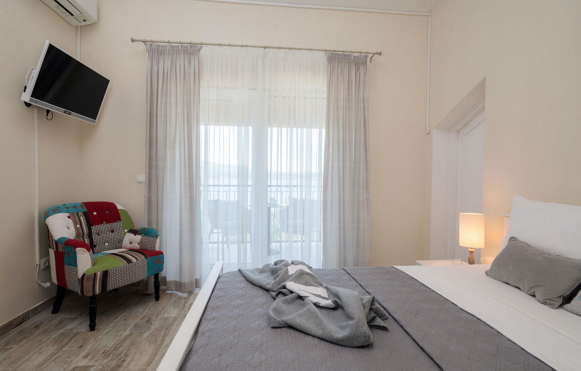 A hotel room with a bed, a chair, a TV, and a window with curtains.