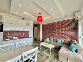 Ein modernes Wohnzimmer mit einer Couch, einem Couchtisch und einer Küchenzeile mit weißen Schränken und einer roten Backstein-Spritzwand.