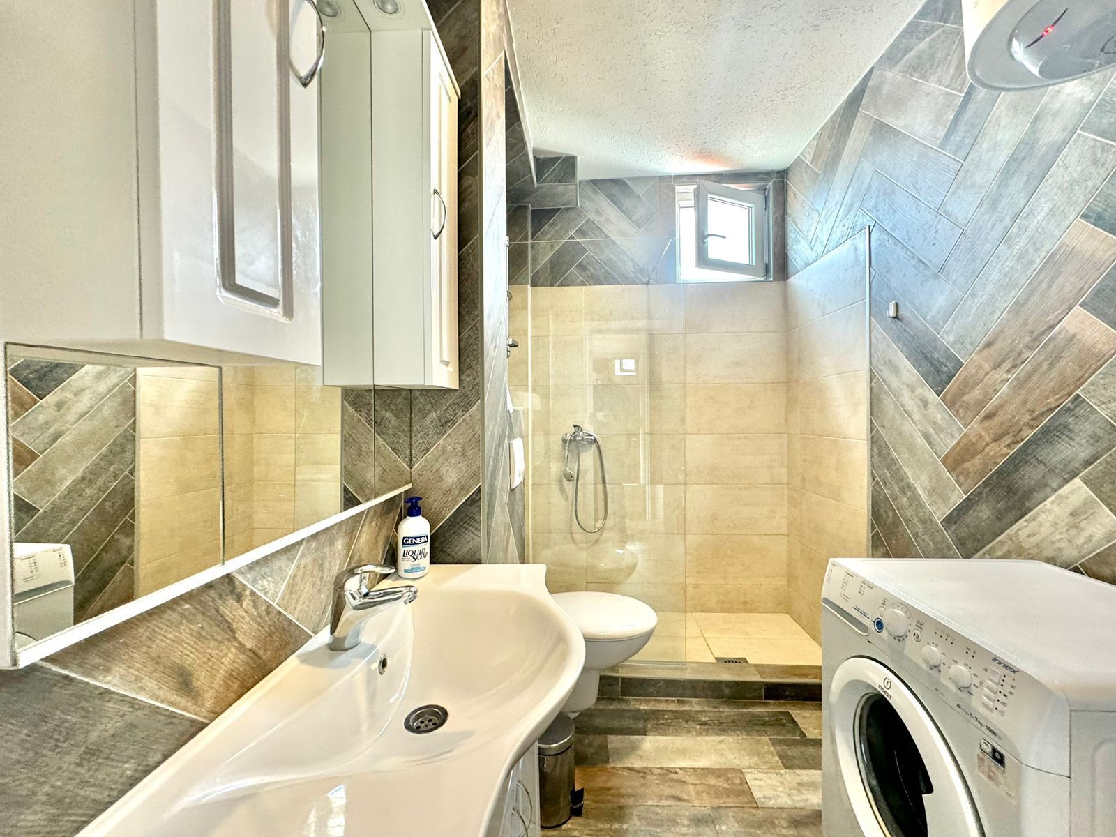 A compact bathroom with a sink, toilet, shower, and washing machine.