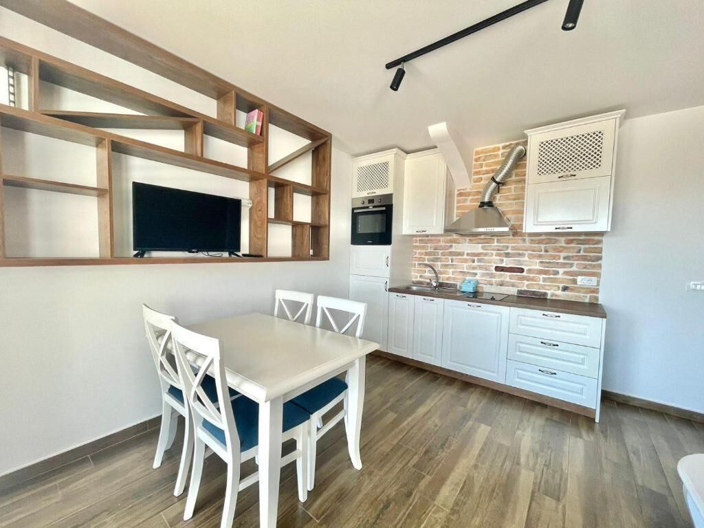 Una cocina moderna con armarios blancos, salpicadero de ladrillo y zona de comedor con mesa y sillas blancas.