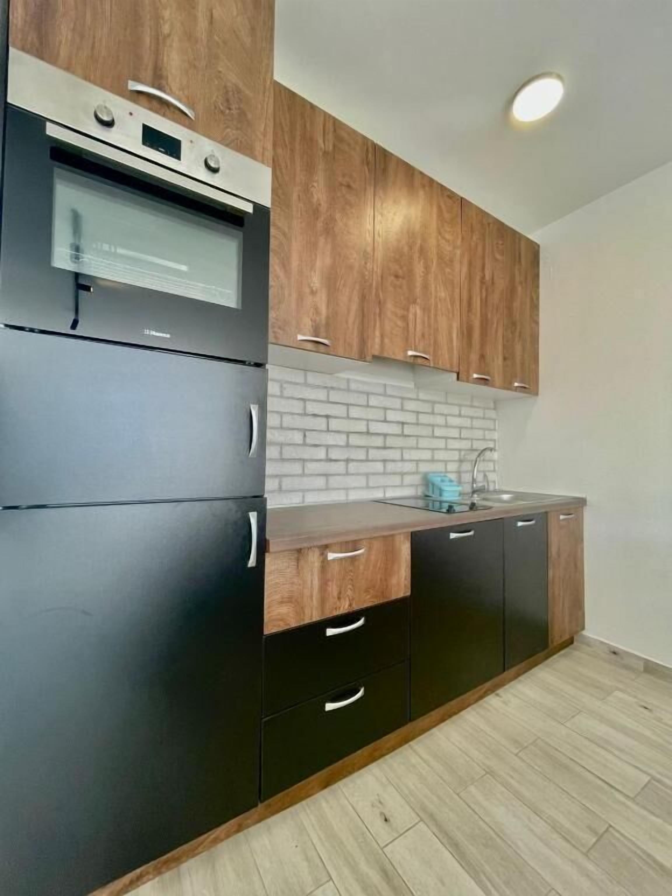 A modern kitchen with black and wooden cabinets, a built-in oven, and a brick backsplash.