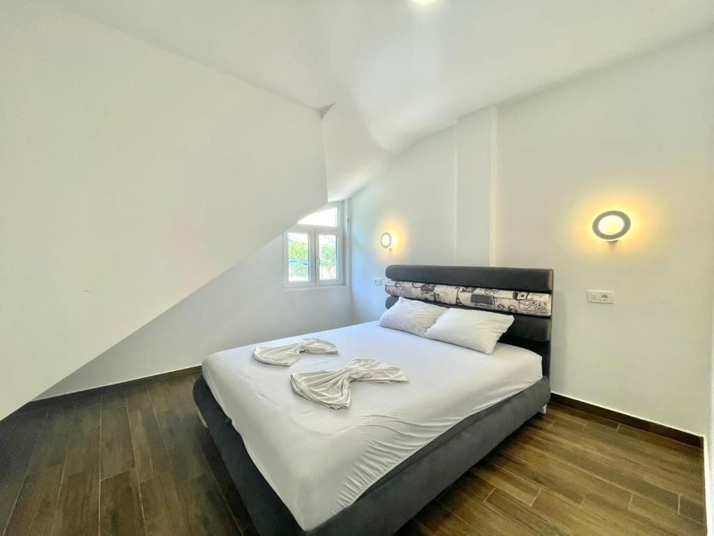 A bedroom with a bed, two wall sconces, a window, and a sloped ceiling.