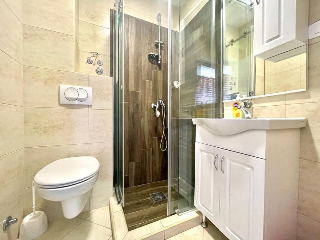 A bathroom with a glass-enclosed shower, a toilet, and a sink with a mirror above it.