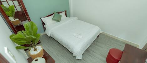 A neatly arranged bedroom with a bed, a mirror, a wooden dresser, and a red stool.