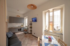 Uma cozinha moderna com armários cinza, uma área de jantar com mesa posta para dois e um espaço de estar acolhedor com sofá.