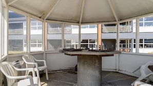Un área de estar al aire libre cubierta con una mesa de hormigón, sillas de plástico blanco y vistas a un edificio con múltiples ventanas.